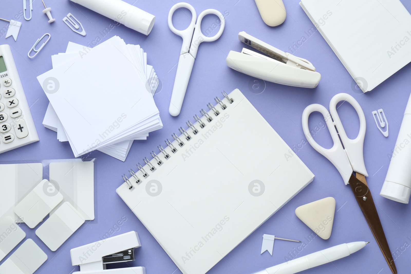 Photo of White notepad and other stationery on violet background, flat lay. Space for text