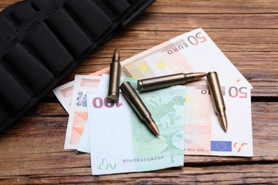 Photo of Metal bullets, euro banknotes and ammunition belt on wooden table, above view