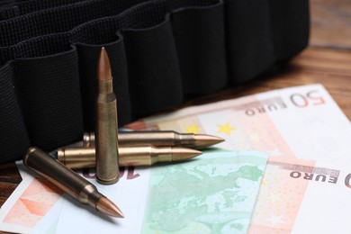 Photo of Metal bullets, euro banknotes and ammunition belt on table, closeup