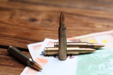 Photo of Metal bullets and euro banknotes on wooden table, closeup