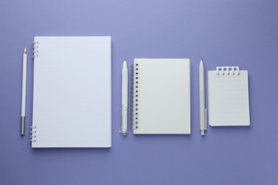 Photo of White notepads and pens on violet background, flat lay. Space for text