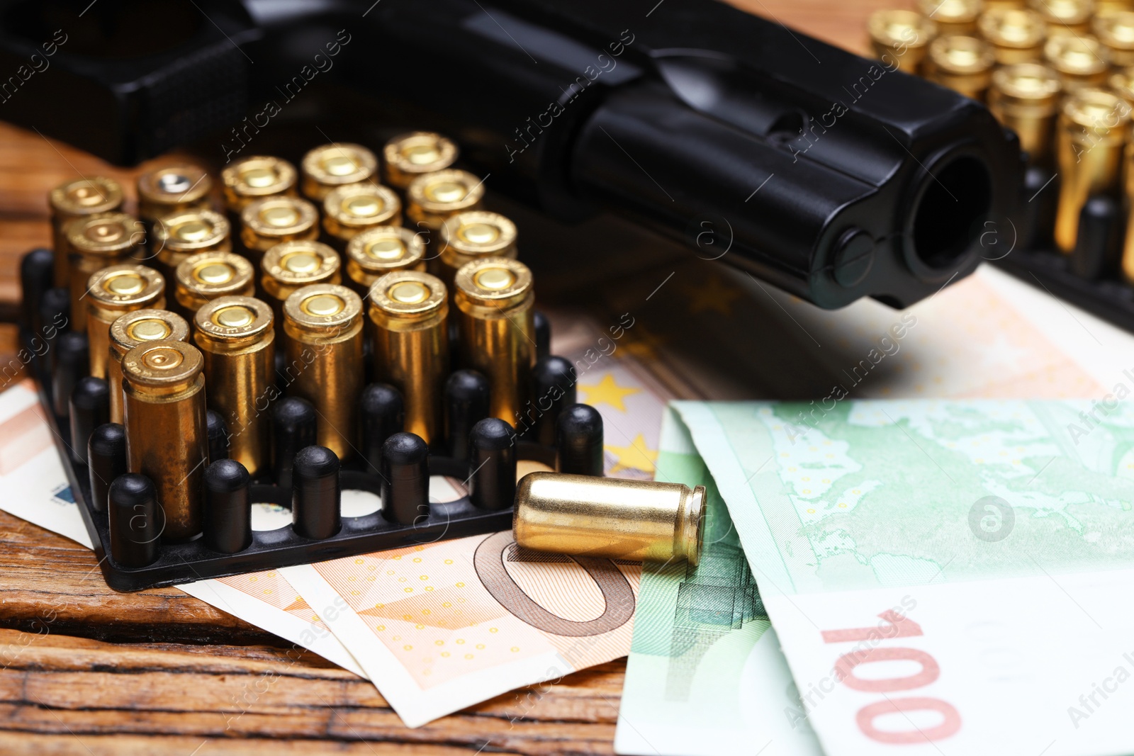 Metal bullets, gun and euro banknotes on wooden table, closeup Photo of Metal bullets, gun and euro banknotes on wooden table, closeup