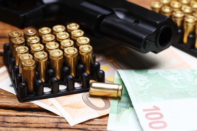 Photo of Metal bullets, gun and euro banknotes on wooden table, closeup