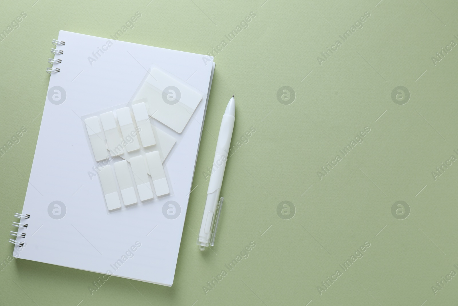 Photo of Open notepad, white pen and sticky tabs on light green background, flat lay. Space for text
