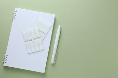 Photo of Open notepad, white pen and sticky tabs on light green background, flat lay. Space for text
