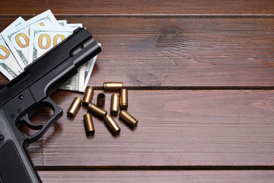 Photo of Bullets, gun and dollars on wooden table, flat lay. Space for text