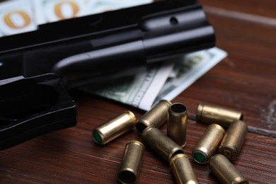 Photo of Bullets, gun and dollars on wooden table, closeup