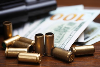 Photo of Bullets, gun and dollars on wooden table, closeup