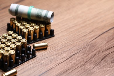 Photo of Bullets and dollars on wooden table, closeup. Space for text