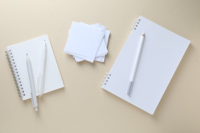 Photo of White notepads, paper notes, pencil and pens on beige background, flat lay
