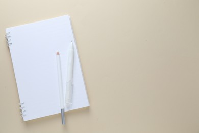 Photo of Open notepad, white pencil and pen on beige background, top view. Space for text