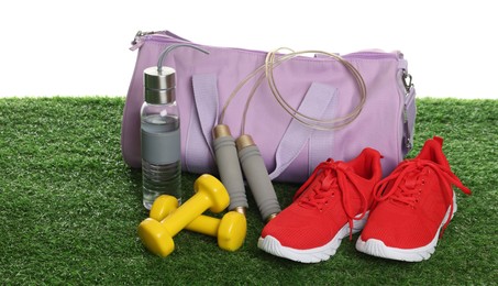 Photo of Stylish sports bag, skipping rope, dumbbells, bottle and sneakers on green grass against white background