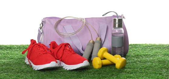 Photo of Stylish sports bag, skipping rope, dumbbells, bottle and sneakers on green grass against white background