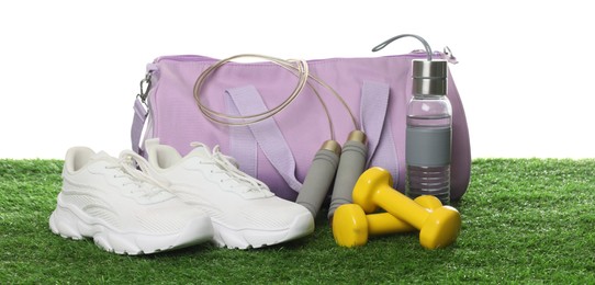 Photo of Stylish sports bag, skipping rope, dumbbells, bottle and sneakers on green grass against white background