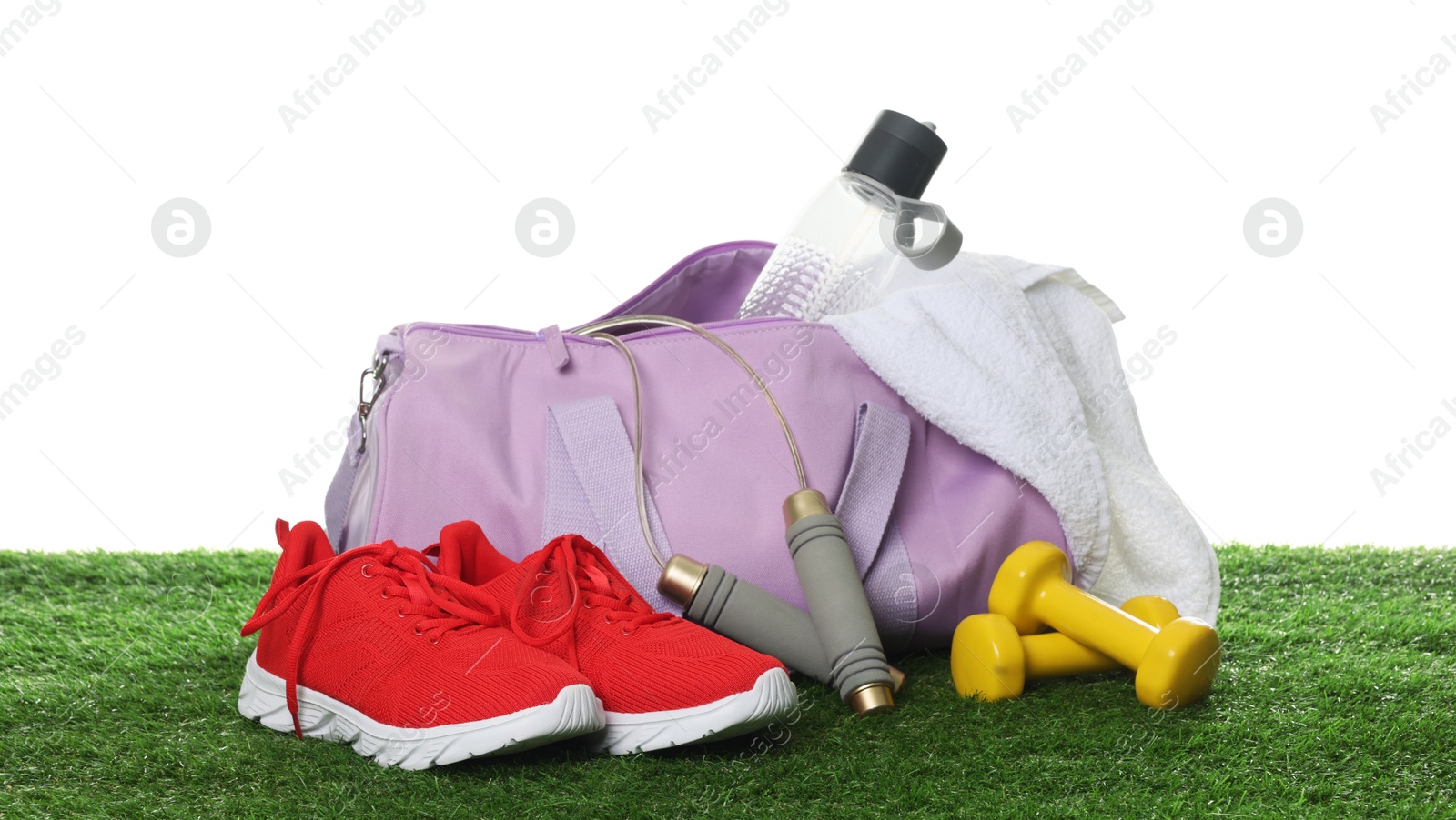 Photo of Stylish sports bag, skipping rope, dumbbells, bottle and sneakers on green grass against white background