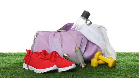 Photo of Stylish sports bag, skipping rope, dumbbells, bottle and sneakers on green grass against white background