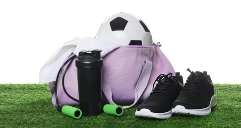 Photo of Stylish gym bag with sports equipment, towel, shaker cup and sneakers on green grass against white background
