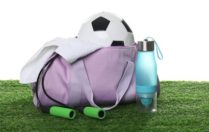 Photo of Stylish gym bag with sports equipment, towel and bottle on green grass against white background