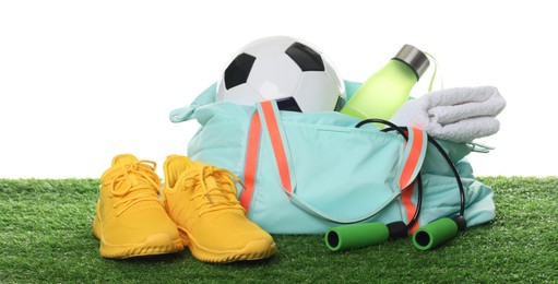 Photo of Stylish gym bag with sports equipment, towel, bottle and sneakers on green grass against white background