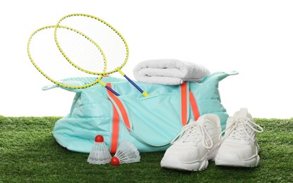 Photo of Stylish sports bag with badminton rackets, shuttlecocks, towel and sneakers on green grass against white background