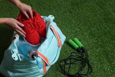 Photo of Woman putting sneakers into stylish sports bag on green grass, closeup