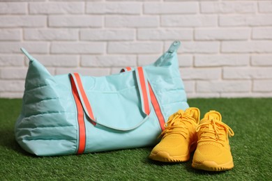 Photo of Stylish sports bag and sneakers on green grass against white brick wall, closeup