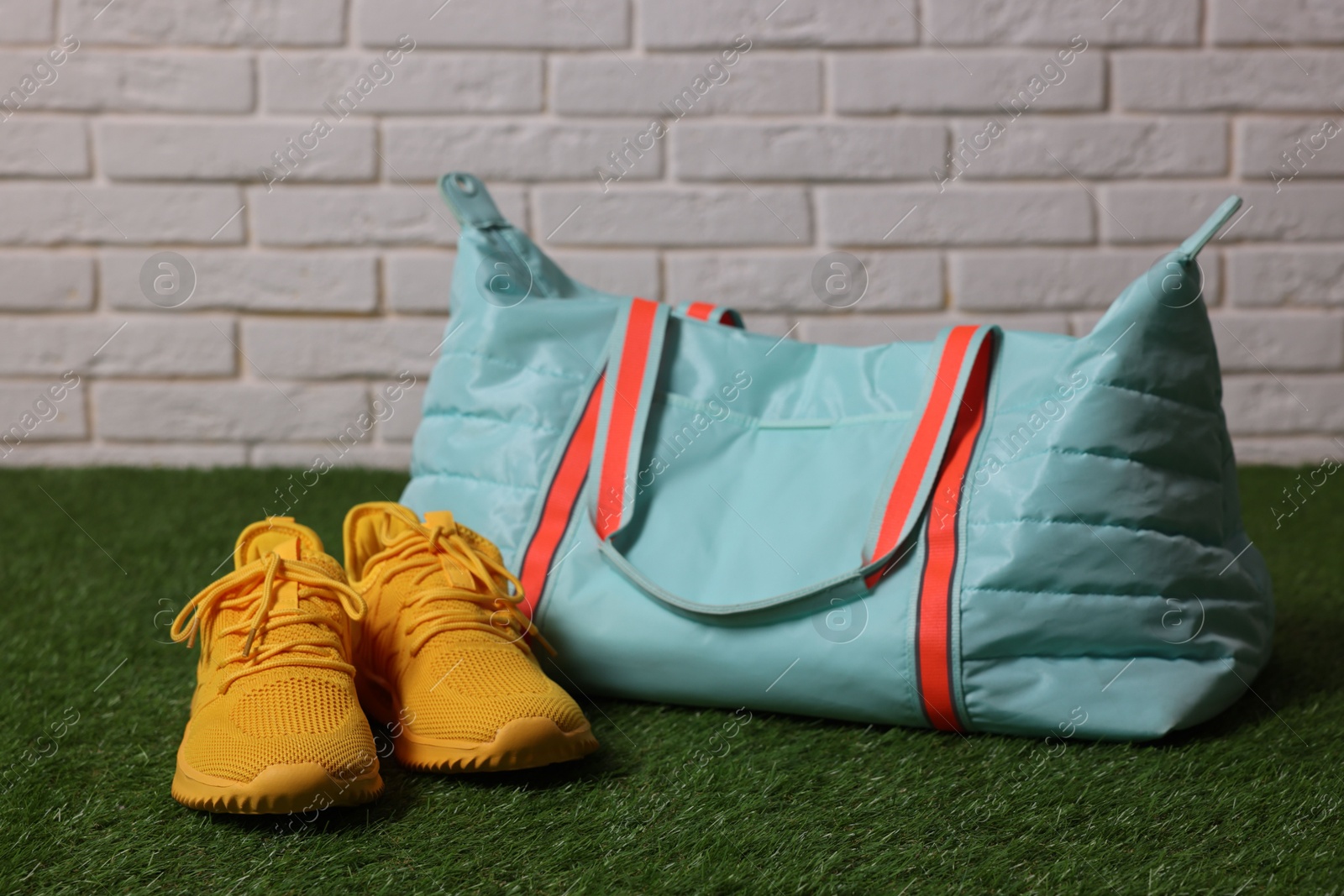 Photo of Stylish sports bag and sneakers on green grass against white brick wall, closeup