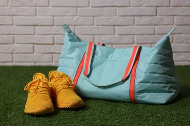 Photo of Stylish sports bag and sneakers on green grass against white brick wall, closeup