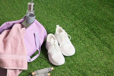 Photo of Stylish sports bag with bottle, towel and sneakers on green grass, closeup. Space for text