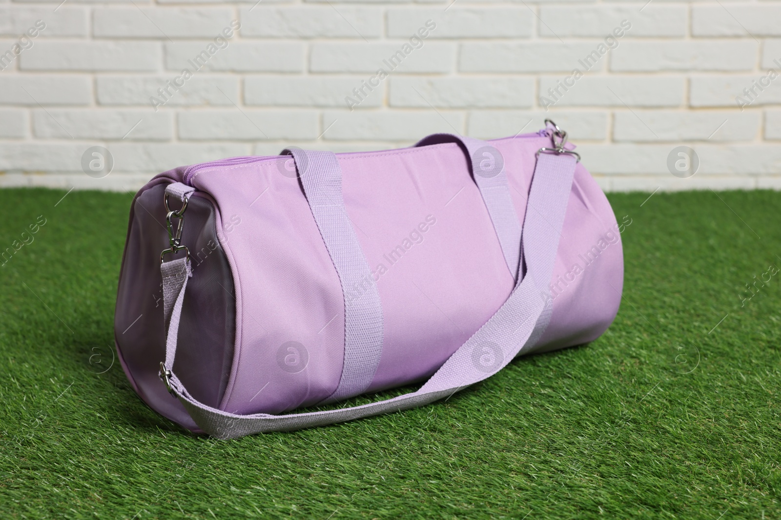 Photo of One stylish sports bag on green grass against white brick wall, closeup