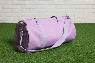 Photo of One stylish sports bag on green grass against white brick wall, closeup