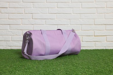 Photo of One stylish sports bag on green grass against white brick wall