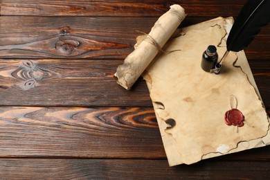 Photo of Old paper scrolls, feather and inkwell on wooden table, flat lay. Space for text