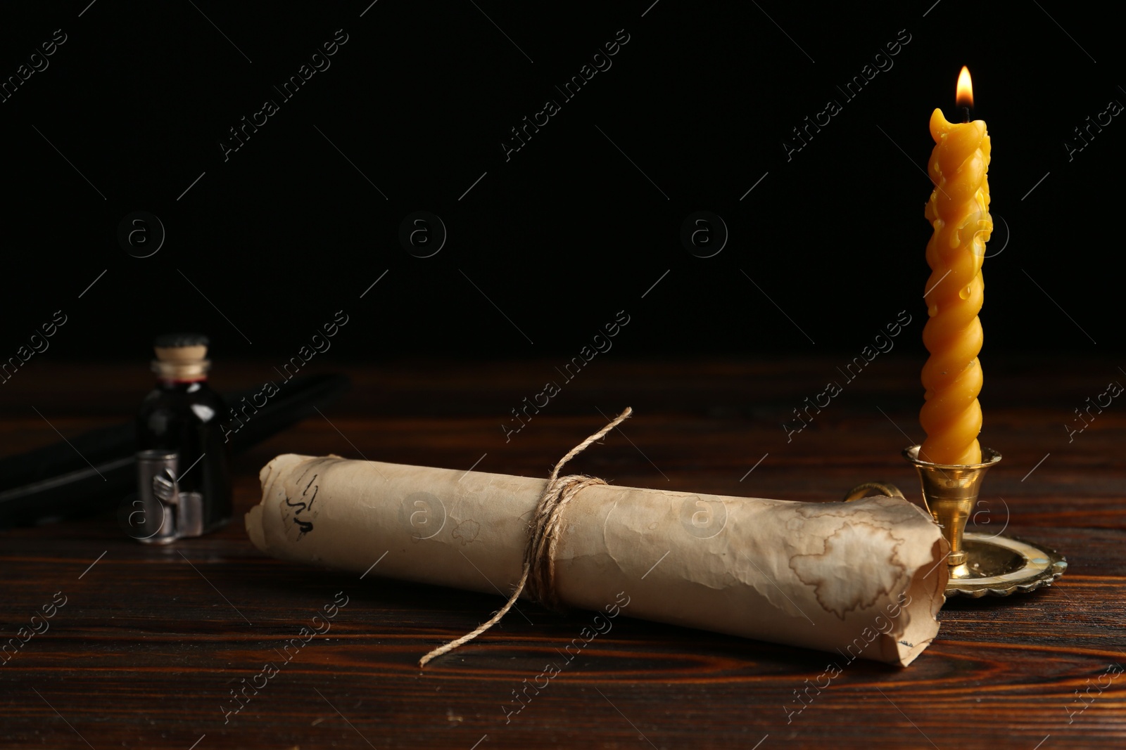 Old paper scroll, feather, inkwell and burning candle on wooden table, closeup Photo of Old paper scroll, feather, inkwell and burning candle on wooden table, closeup
