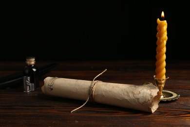 Photo of Old paper scroll, feather, inkwell and burning candle on wooden table, closeup