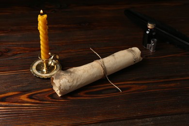 Photo of Old paper scroll, feather, inkwell and burning candle on wooden table, closeup