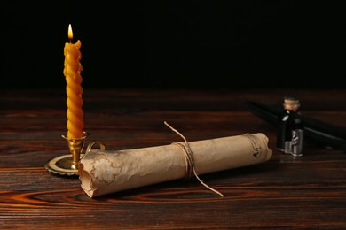 Photo of Old paper scroll, feather, inkwell and burning candle on wooden table, closeup