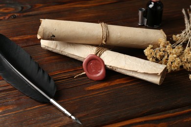Photo of Old paper scrolls and feather on wooden table, closeup