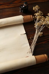 Photo of Old rolled scroll, dry flowers and inkwell on wooden table, above view