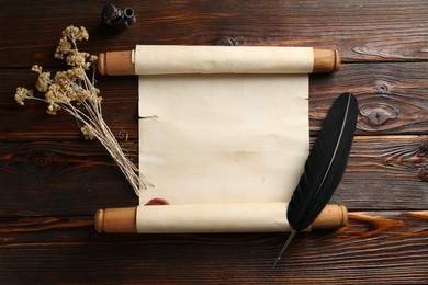 Photo of Old rolled scroll, feather, dry flowers and inkwell on wooden table, flat lay