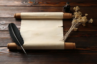 Photo of Old rolled scroll, feather, dry flowers and inkwell on wooden table, above view