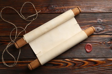 Photo of Old rolled scroll, wax seal and twine on wooden table, flat lay