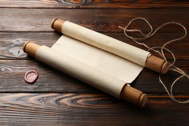 Photo of Old rolled scroll, wax seal and twine on wooden table, closeup