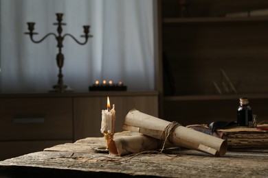 Photo of Old paper scrolls, book, feather, inkwell and burning candle on wooden table