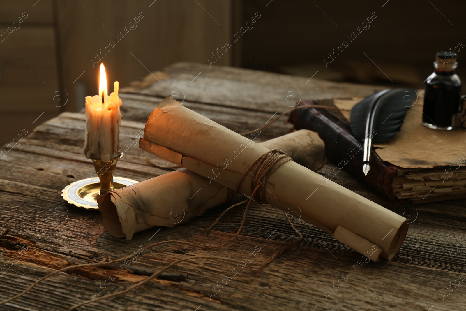 Old paper scrolls, book, feather, inkwell and burning candle on wooden table, closeup Photo of Old paper scrolls, book, feather, inkwell and burning candle on wooden table, closeup