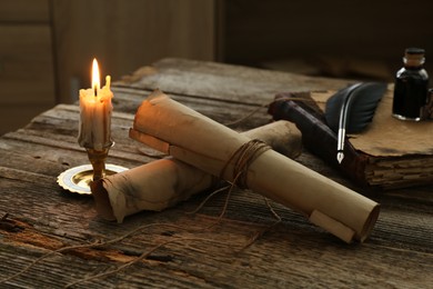 Photo of Old paper scrolls, book, feather, inkwell and burning candle on wooden table, closeup