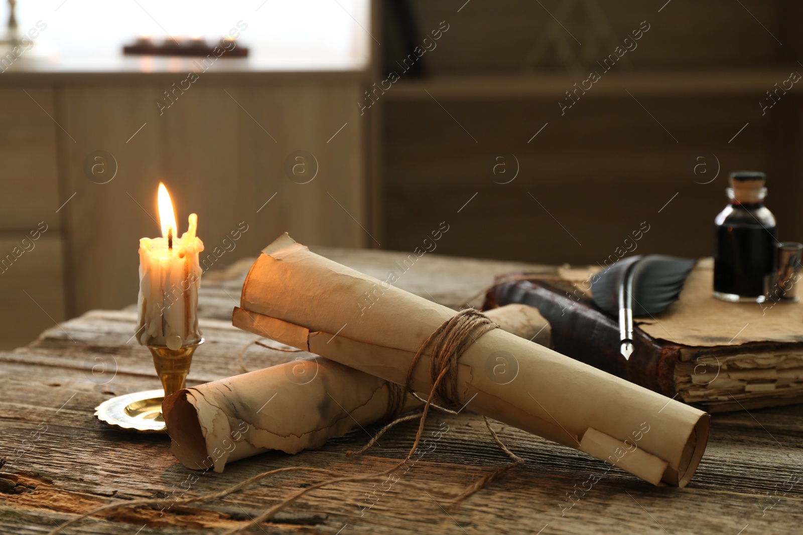 Old paper scrolls, book, feather, inkwell and burning candle on wooden table, closeup Photo of Old paper scrolls, book, feather, inkwell and burning candle on wooden table, closeup