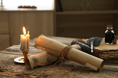 Photo of Old paper scrolls, book, feather, inkwell and burning candle on wooden table, closeup