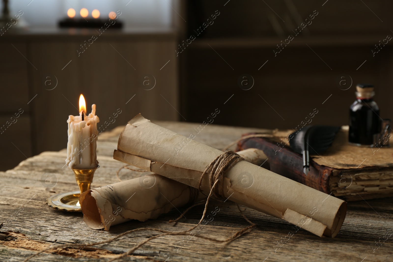 Old paper scrolls, book, feather, inkwell and burning candle on wooden table, closeup Photo of Old paper scrolls, book, feather, inkwell and burning candle on wooden table, closeup