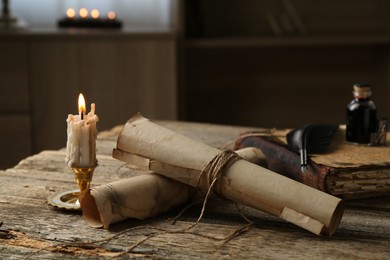 Photo of Old paper scrolls, book, feather, inkwell and burning candle on wooden table, closeup